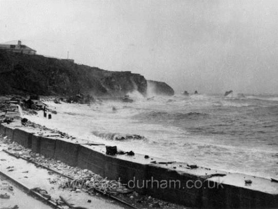 B&W photo of coastline with large waves crashing on cliffs to the left of the image.