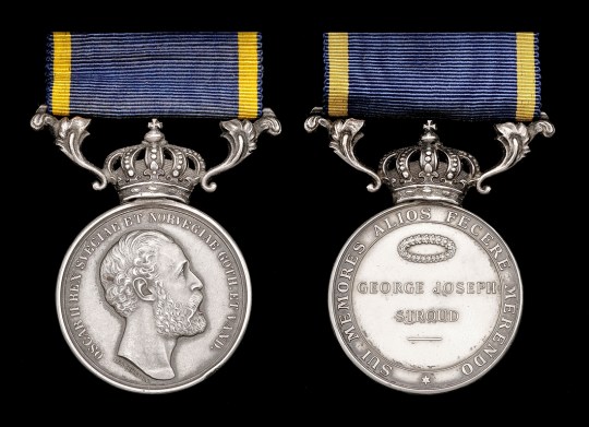 Colour photo of two sides of silver medal on black background, suspended from crown and blue and yellow ribbon. To left, profile of bearded man surrounded by Latin inscription; to right Right side: recipient’s name GEORGE JOSEPH STROUD underneath a wreath, also surrounded by a Latin inscription. 