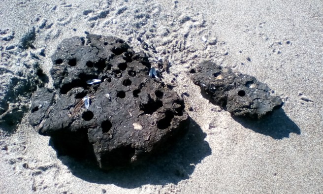 Two fragments of dark brown peat, one large on left, smaller fragment to centre right, on sand