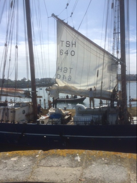 Colour photo of a schooner's sail being lowered between two masts as she ties up at a quayside.
