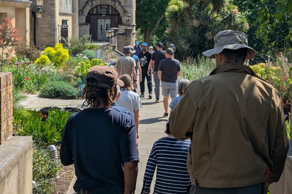 A crowd walk towards the Horniman clocktower. A man and a woman in the foreground wear a hat.