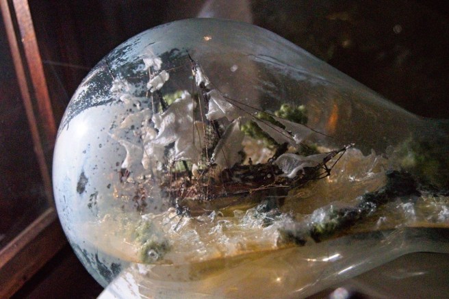 Modern colour close-up view of 'shipwreck in a bottle' showing the structure of the vessel and the build up of glue creating the waves inside the bottle.