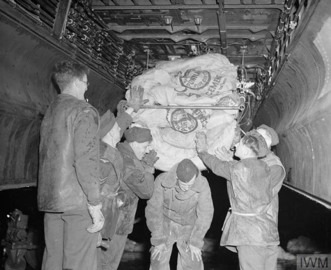 Historic B&W photo of six men loading the sacks, their uniforms streaked with escaped flour.