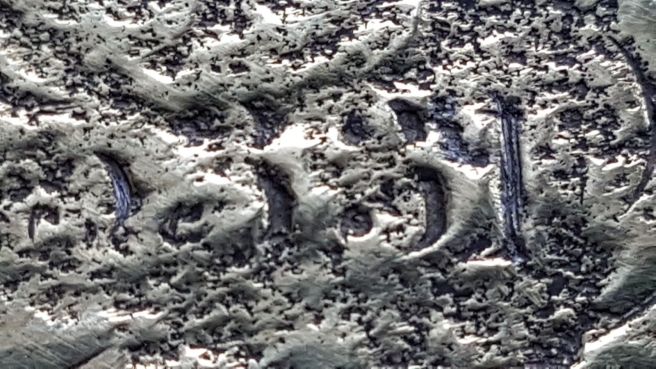 Detail view of corroded and pitted metal in which the numbers 5 3 3 1 are just legible.