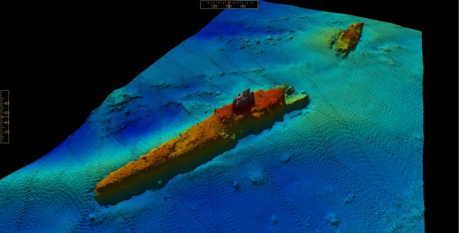 Multibeam image of wreck on seabed, with blues representing depths, greens areas of sandbank, and reds the upstanding wreck structure, broken in two, orientated lower left to upper right of image.