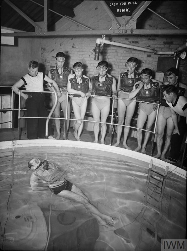 Historic B&W photograph of man wearing the apparatus in a tank while the trainees watch.