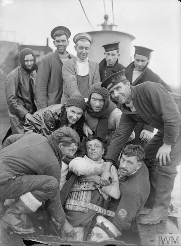 Historic B & W photograph of men surrounding a survivor in a cork lifejacket.