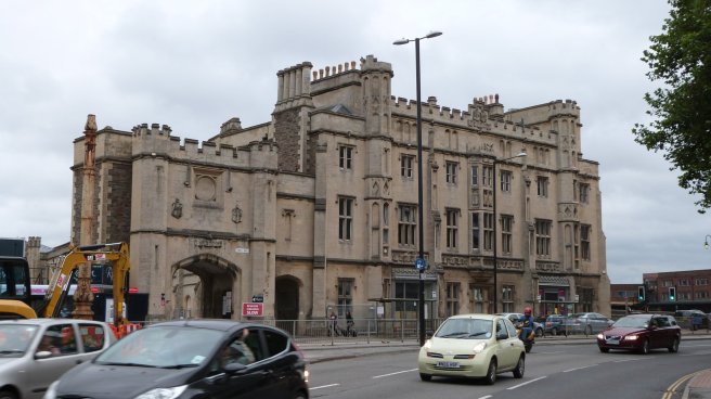Modern colour photograph, Brunel's old station now beside a busy road with plenty of car traffic. The front elevation is built of cream limestone but areas behind, such as the side returns and chimney stacks, are built of less prestigious and darker Pennant stone.
