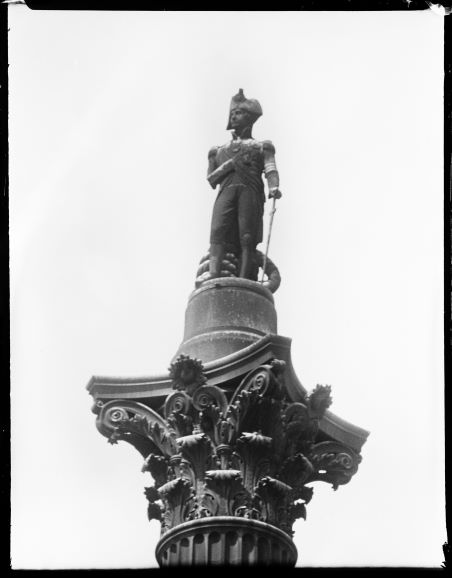 Black and white photo close up view of statue of Nelson, atop the capital of the column with ornamental leaf design