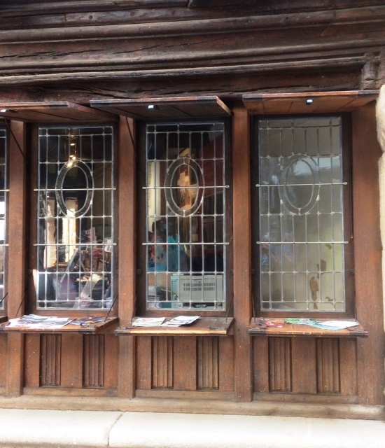 Modern colour photo of 3 glass windows set in a timber building, with horizontal shutters open above and below the windows, the lower shutters acting as counters (used to display literature on the building, formerly as a shop).