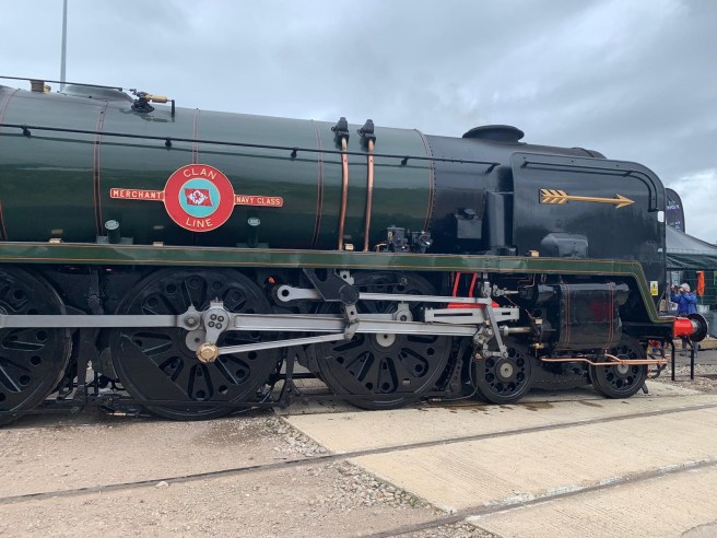 Steam locomotive in green and black livery with a Golden Arrow on its side (to right of image) and the prominent Clan Line Merchant Navy Class logo, enclosing the line's house flag of a red lion rampant