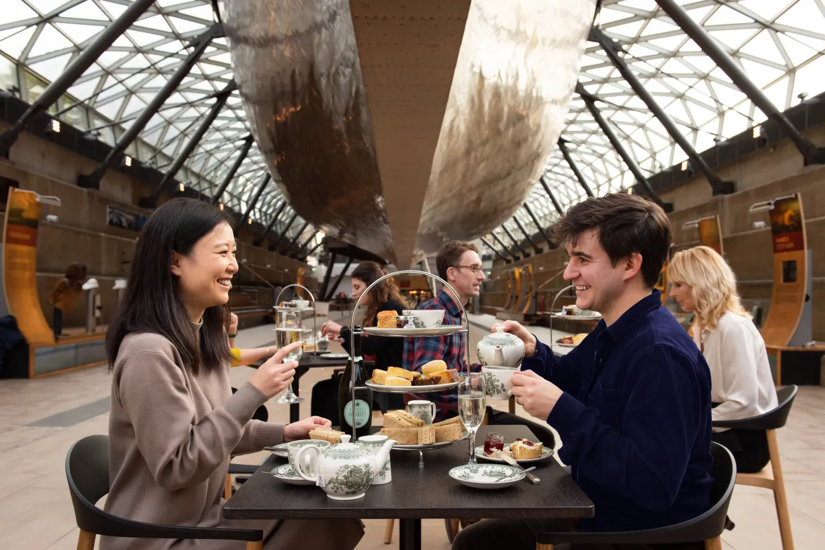 A couple enjoy afternoon tea under the raised hull of historic ship Cutty Sark.