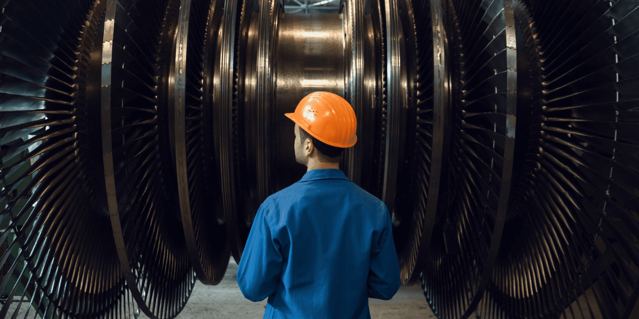 Man In Orange Hard Hat Looking At Large Metal Wheels