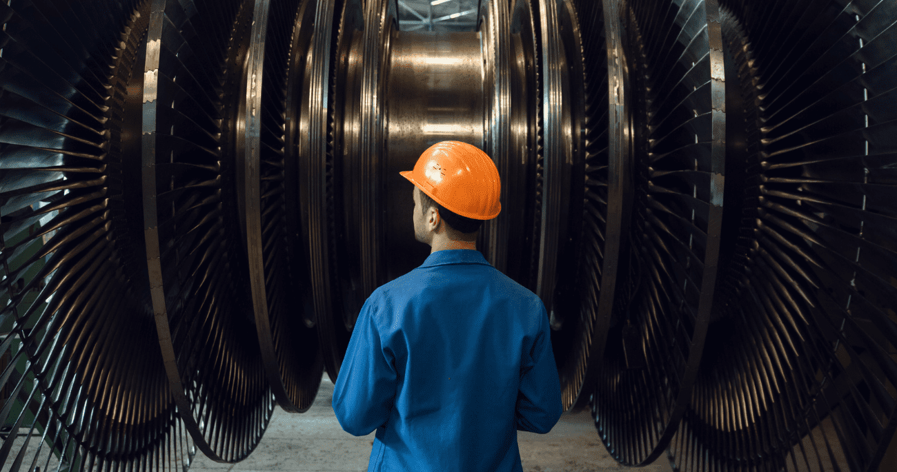 Man In Orange Hard Hat Looking At Large Metal Wheels