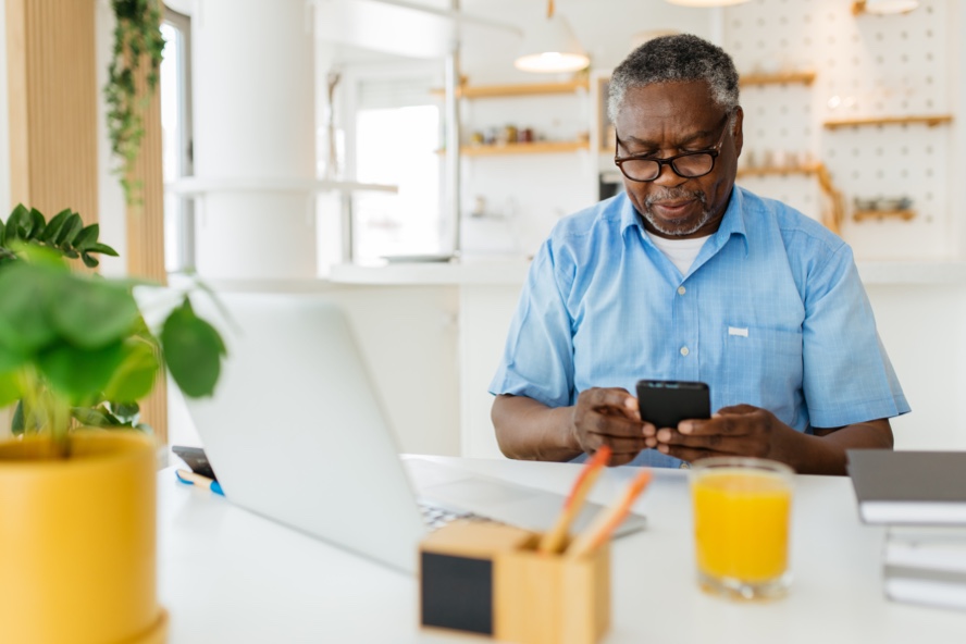 Man sitting at his home office and using his phone in front of his laptop