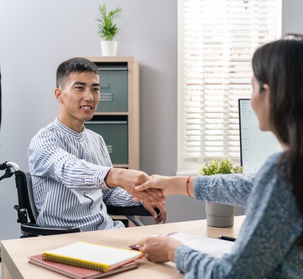 Man in wheelchair shaking hands with a woman over a desc