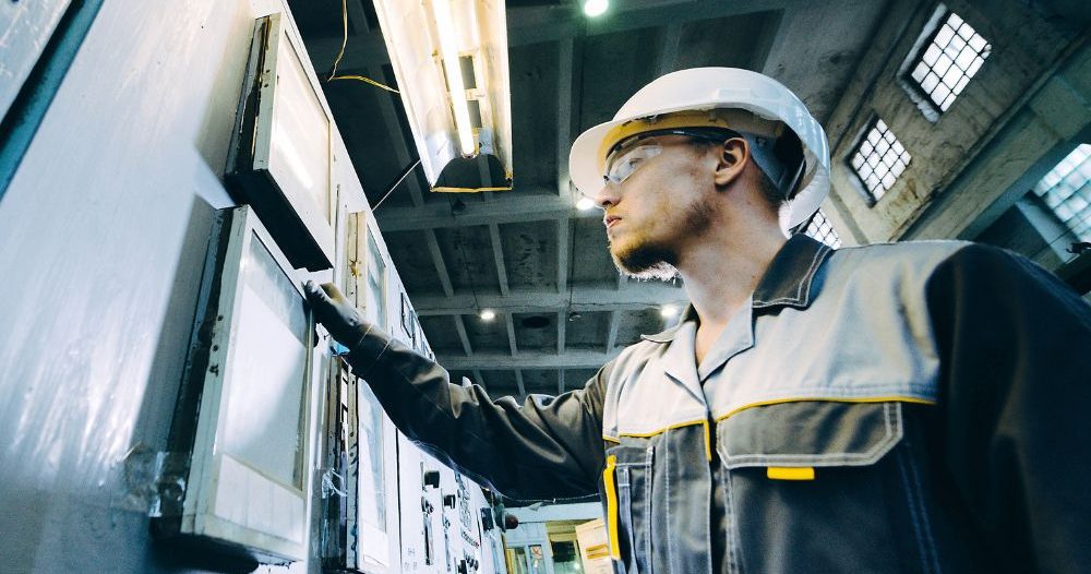 A Person In A Hard Hat Standing In Front Of A Control Panel
