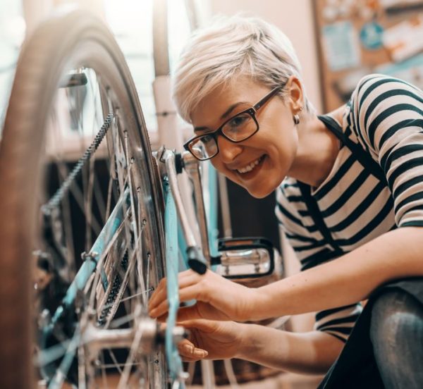 Woman in overalls smiling while fixing a bicycle