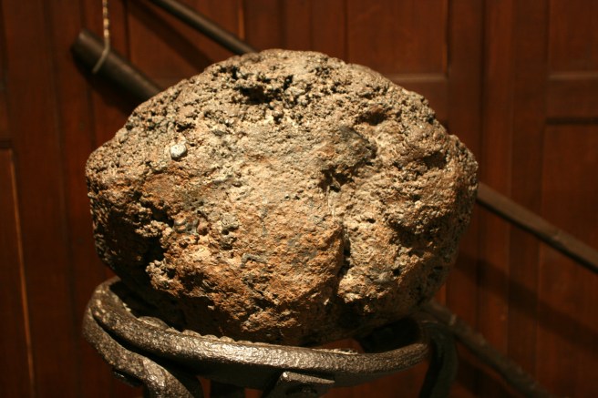 Lump of grey iron on a stand in a museum display, against a brown wooden background.