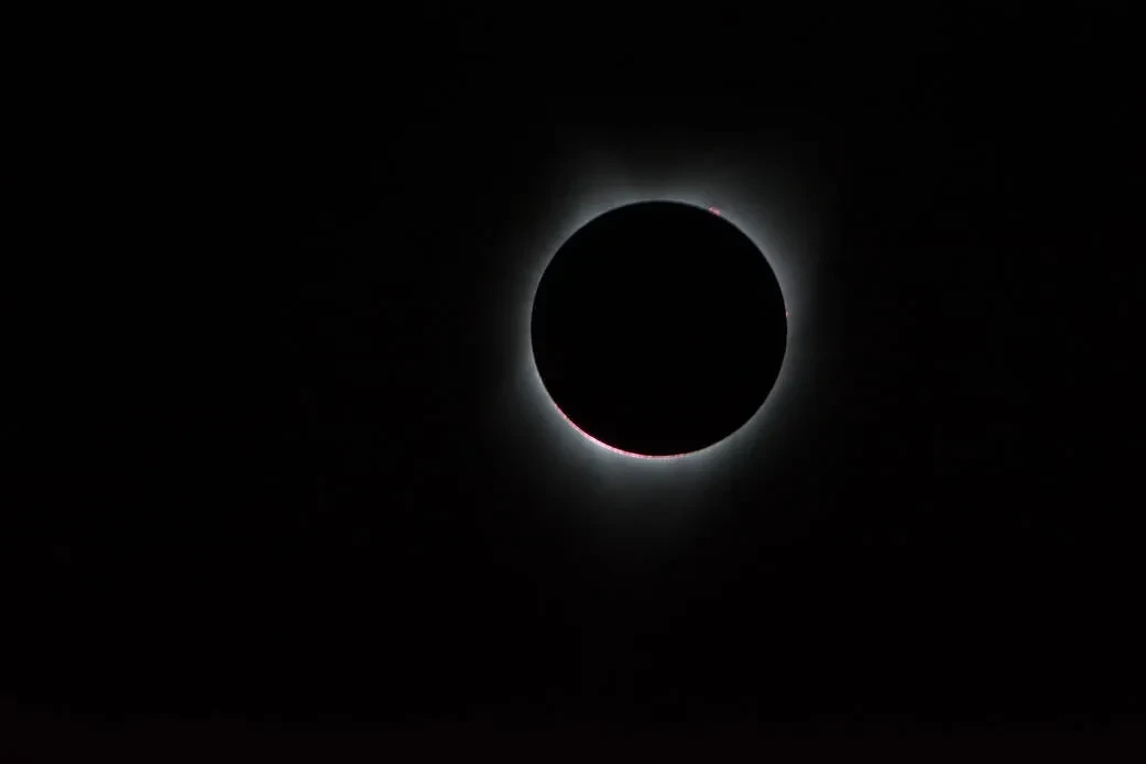 Image of the Sun with the Moon in front of it, with solar corona coming out from behind the circular Moon