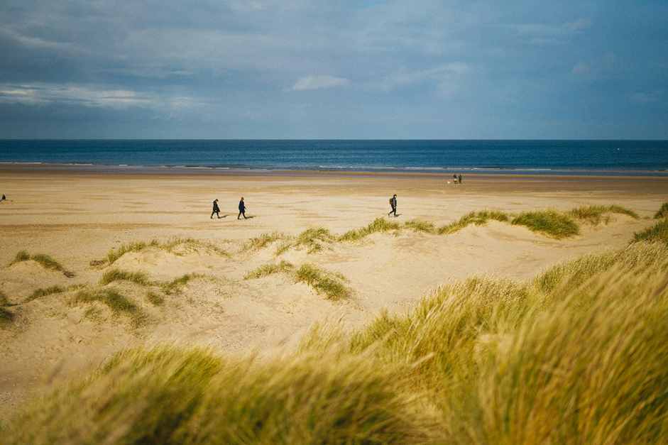 Landscape photo of sand dunes featuring people walking on the beach