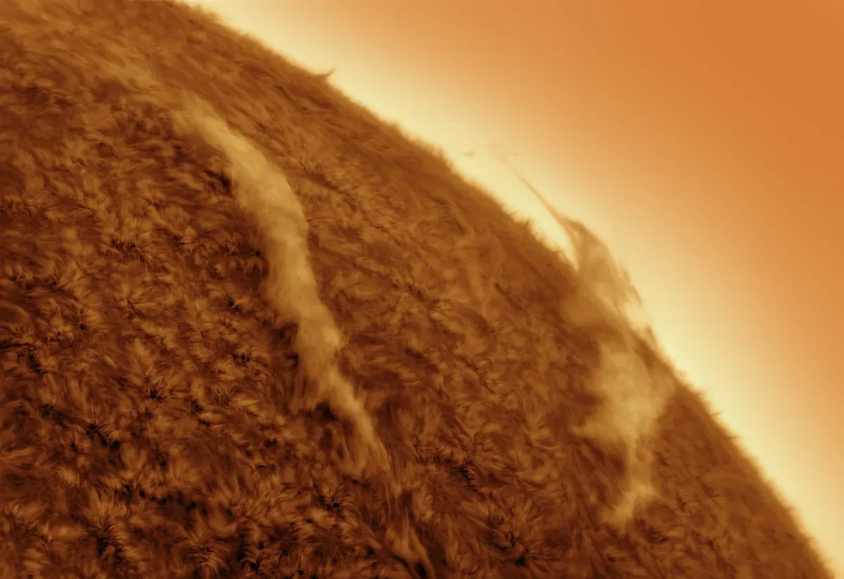 Close up of a section of the Sun's limb. Golden swirls make up the Sun's surface and there are two thin clouds of plasma in a lighter colour above the surface
