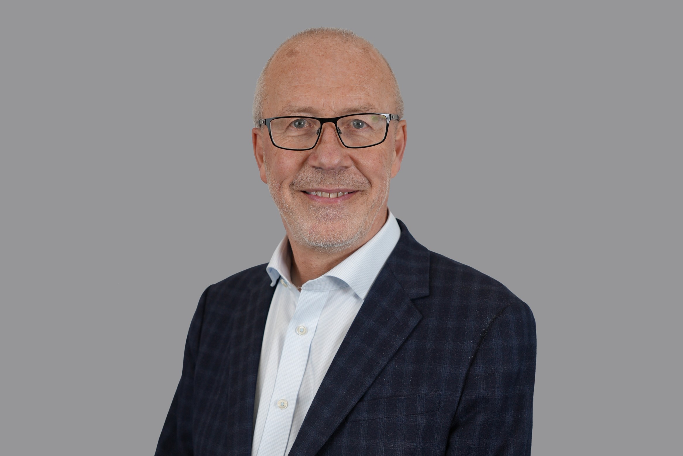 Professional headshot of person wearing glasses, shirt and smart jacket against a studio background, looking at camera.