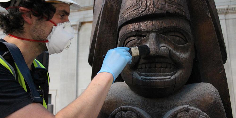 Conservator Jamie Hood removing dust from the Haida totem pole in the Great Court.