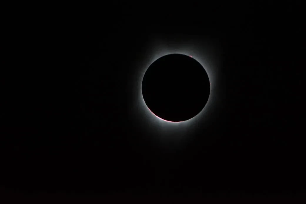Image of the Sun with the Moon in front of it, with solar corona coming out from behind the circular Moon