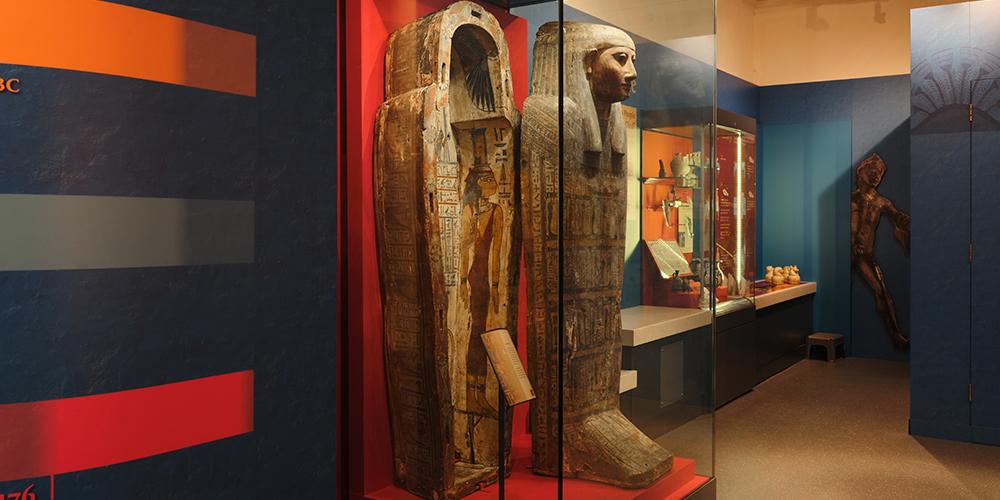 Internal view of a museum gallery showing objects including Egyptian coffins. 