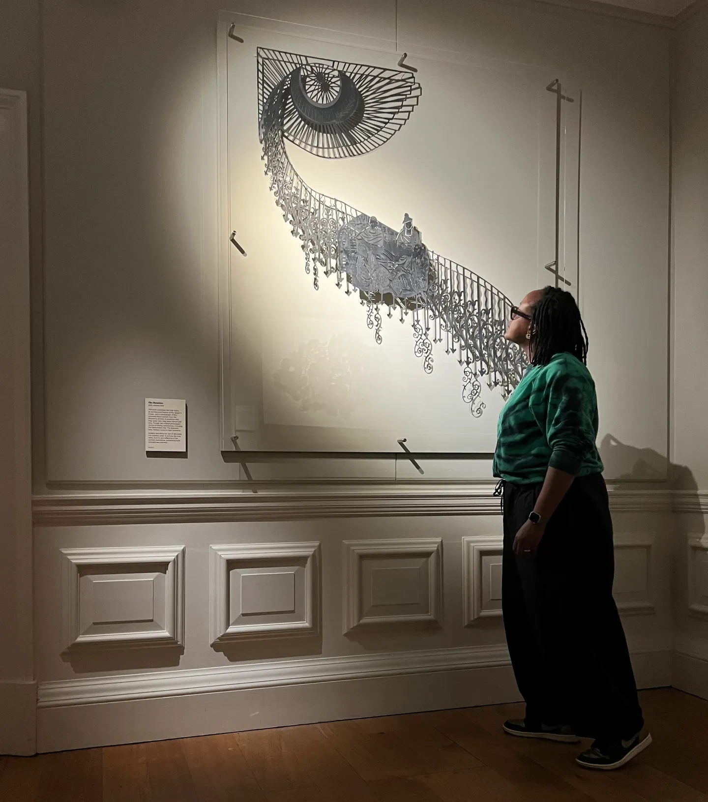 Artist Sharon Walters stands in front of an artwork featuring a historic photograph of four women placed against an iron staircase