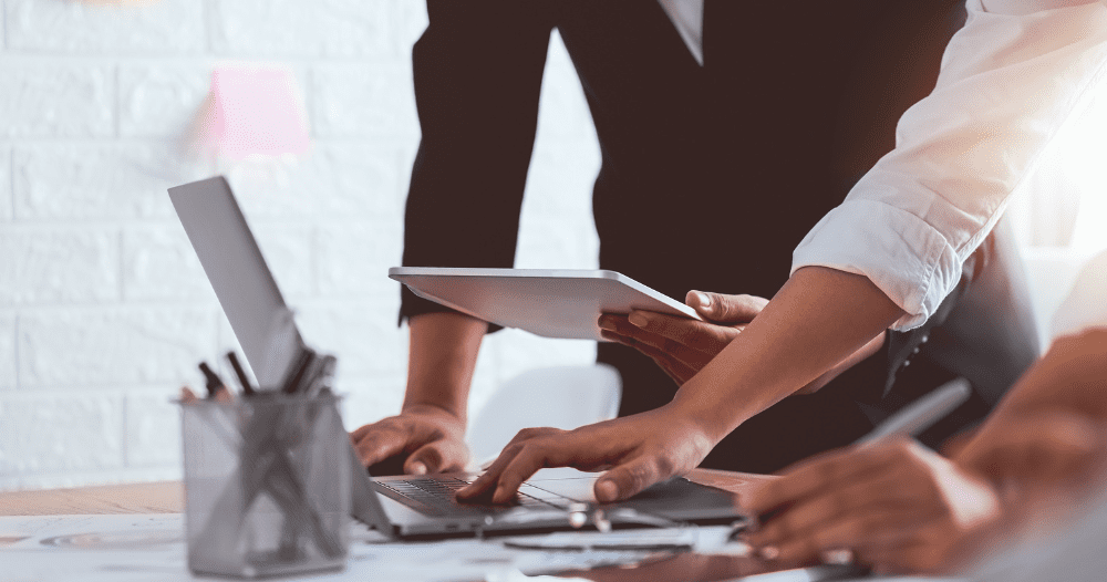Two People Standing And Working On A Lap Top At A Desk