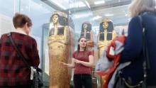 A tour guide speaking to visitors in front of an Egyptian mummy case. 