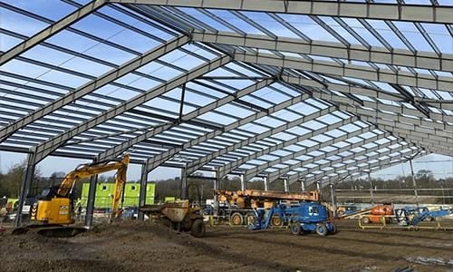 View of a steel beam structure at a construction site with ongoing heavy machinery work.