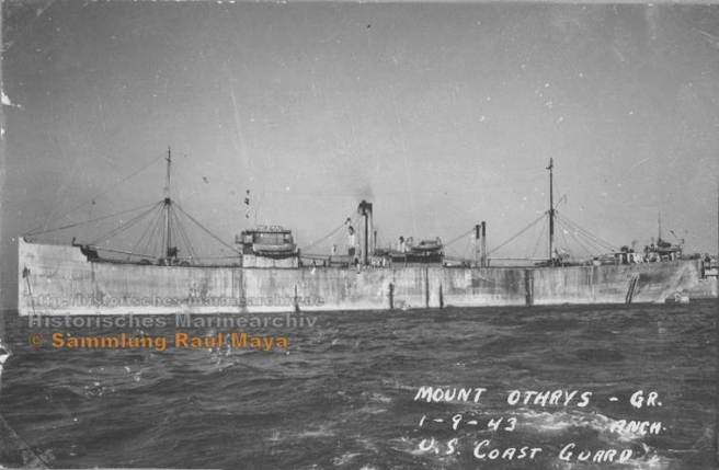 Black and white photograph of the SS Mount Othrys, a Greek cargo vessel, in the water. The ship is shown with masts and cargo equipment visible, taken from the side with some coastline in the background.