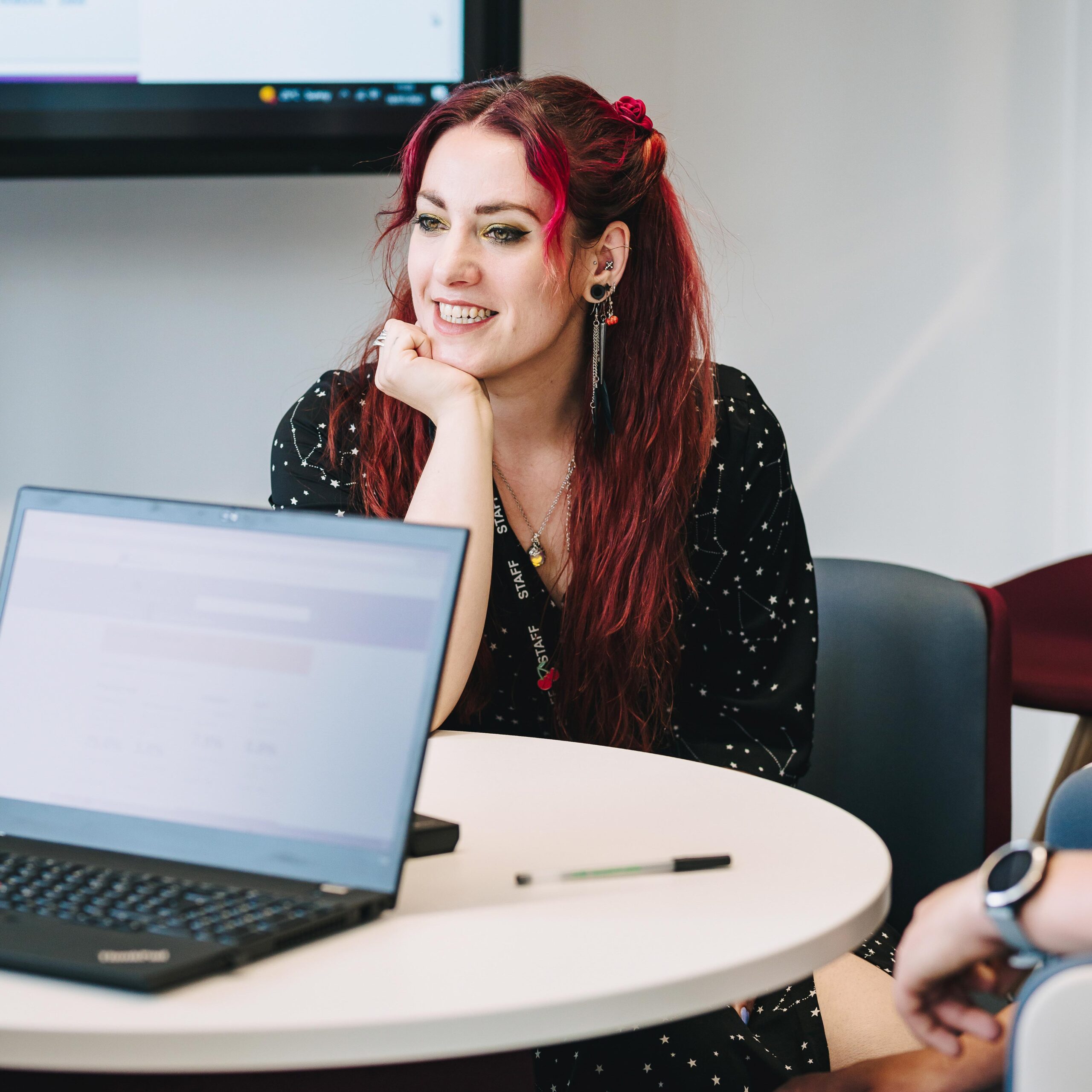 Young woman smiles at collegue, in the foreground is a laptop sits open.