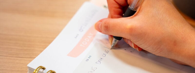 A ring bound planner with a hand holding a pen writing the words 'ONS DAY ONE!