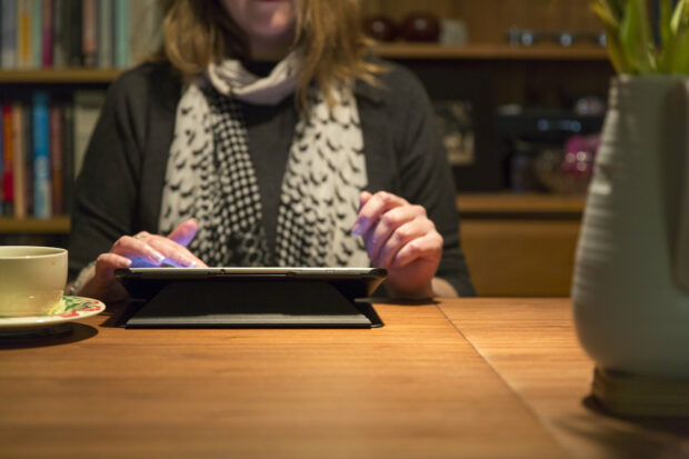 A woman sitting at a table in her home reading content on GOV.UK using a tablet device