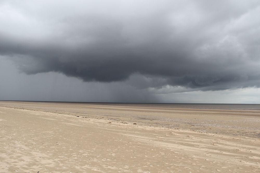 Stormy dark grey clouds over a light sandy beach