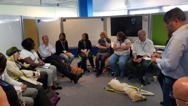 A group of delegates sitting in a circle having a discussion. A guide dog is asleep on the floor