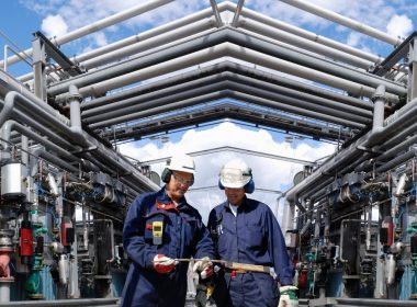 Two Men On Site Walking Below Pipes