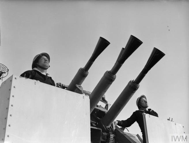 Two men stand either side of four cannon pointing right and upwards to the sky