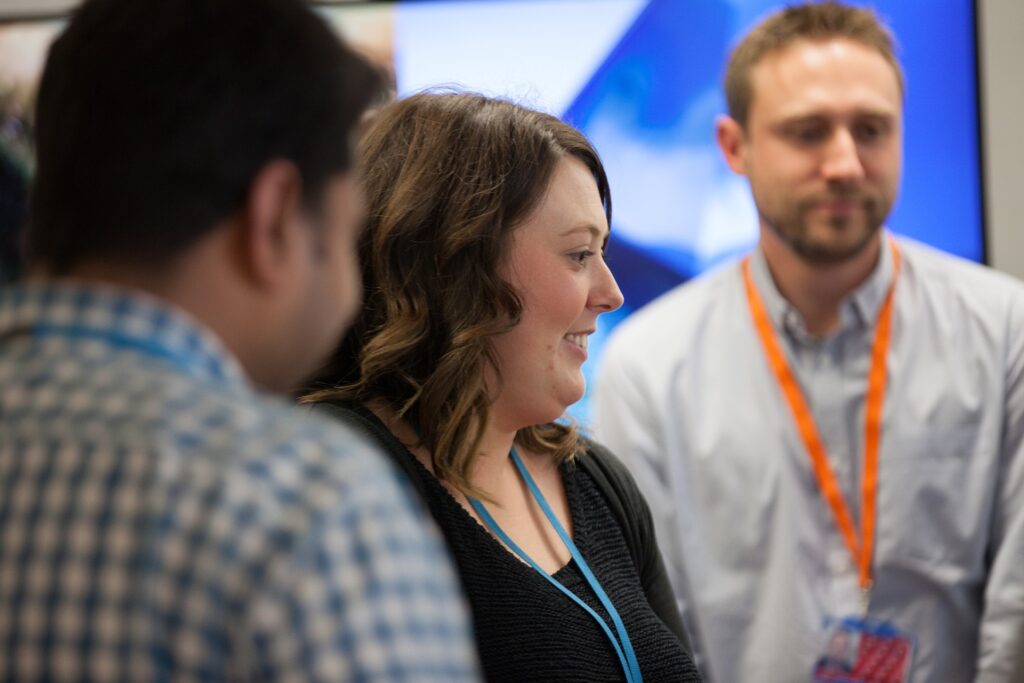 Two males and a female standing in an open plan office looking at something out of shot