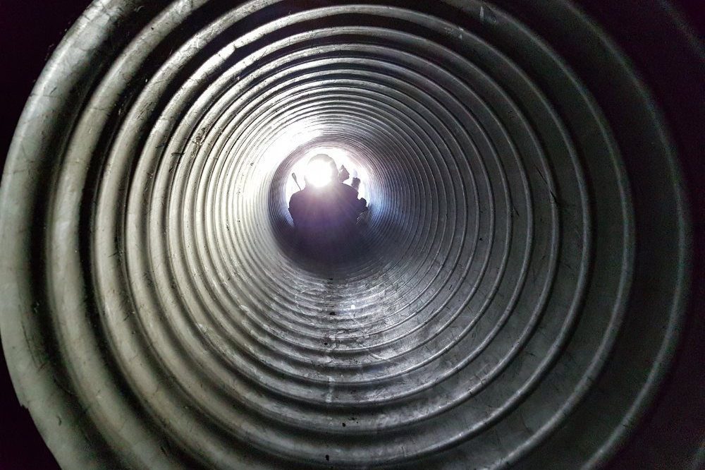 Person With Torch Looking Through Metal Pipe Tube