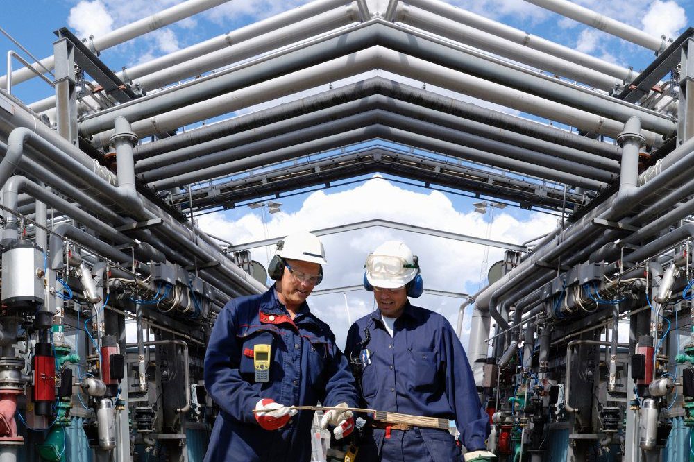 Two Men On Site Walking Below Pipes