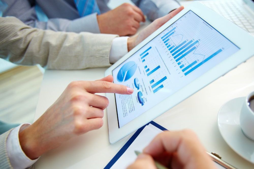 Group Of People Reading Tablet With Graphs On It