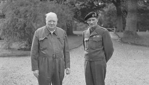 The Prime Minister Winston Churchill, wearing his siren suit, poses with Field Marshal Bernard Montgomery on 19 May 1944 during a tour of forces preparing to invade Normandy.