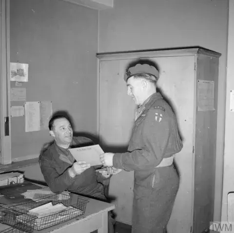 A British Army soldier collects his demobilisation documents from a colleague who is sat behind a desk.