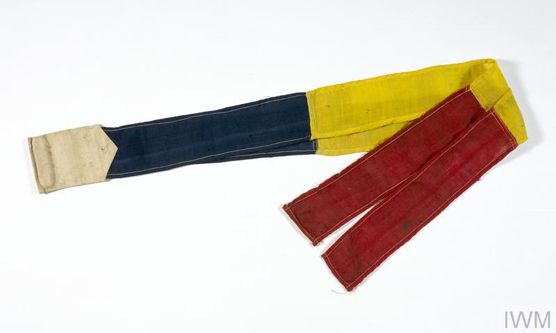 Message streamer of cotton, presented in two strips of segmented blue, yellow and red with beige stitching.