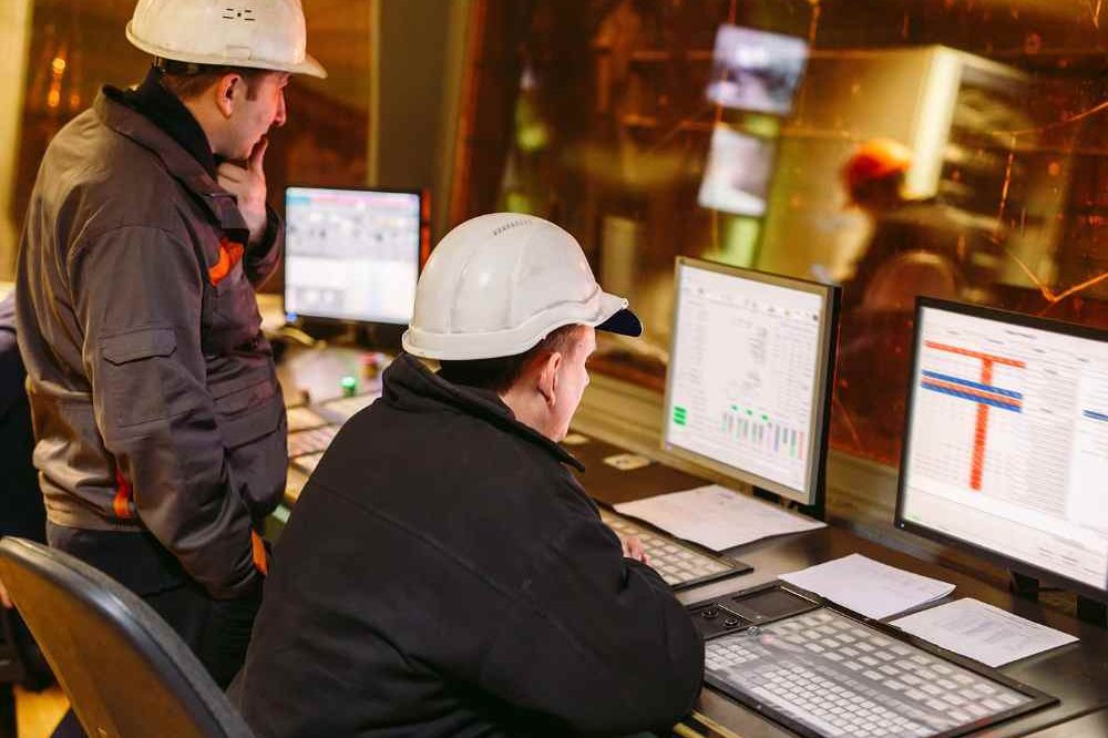 Two Men In White Hard Hats Working At A Controls Panel